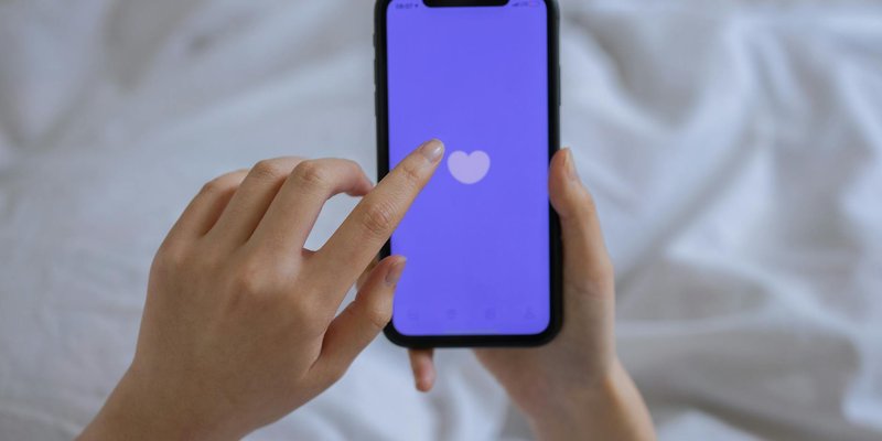 Close-up of hands using a smartphone with a heart icon on screen, representing technology and connec