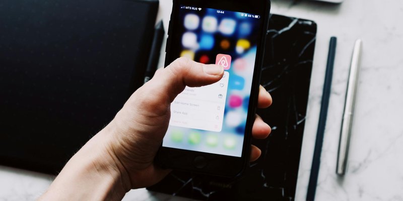 A person holds a smartphone displaying app icons over a desk with digital tablets and pens.