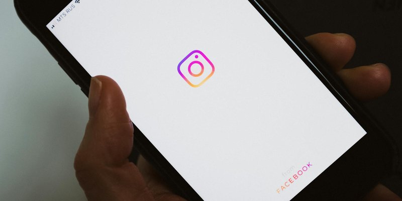 Crop faceless person taking mobile phone and demonstrating blank screen with social media app logo w