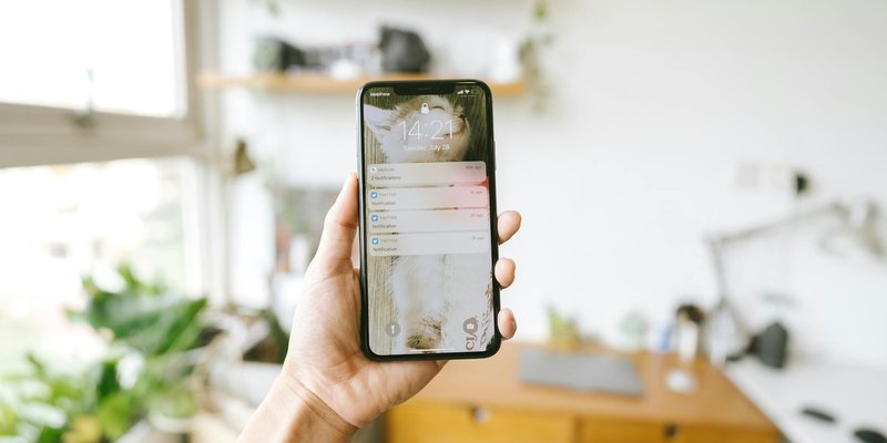 Hand holding smartphone indoors with blurred office background, focus on screen notifications.