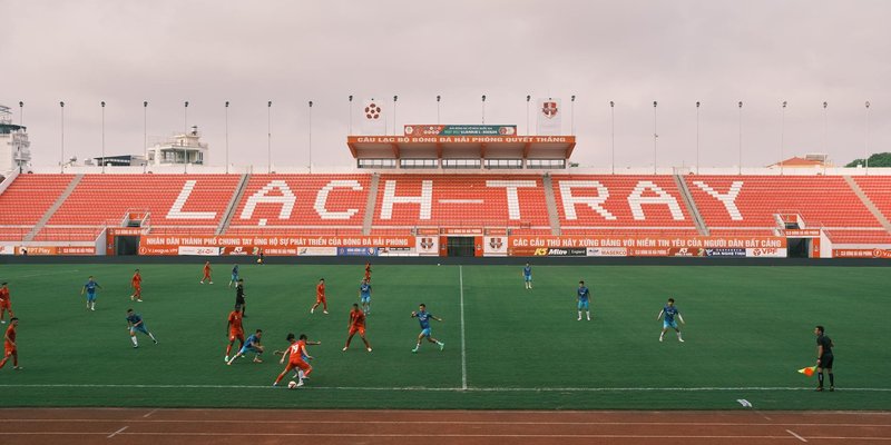 Players engaged in a soccer match at Lạch Tray Stadium, Hải Phòng, Vietnam. Cloudy day setting.