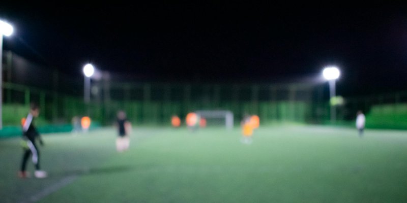 Blurred image of a nighttime football match under bright stadium lights with players on the field.