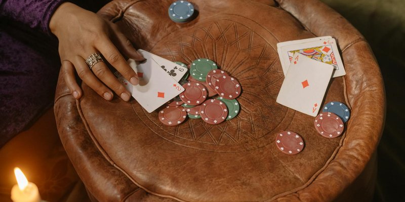 A hand playing cards on a leather table with poker chips and a candle.
