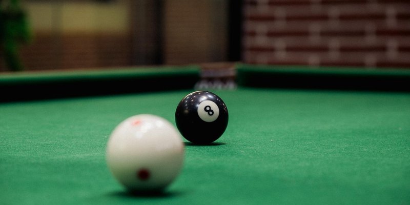 Focused shot of a black eight ball and a white cue ball on a pool table indoors.