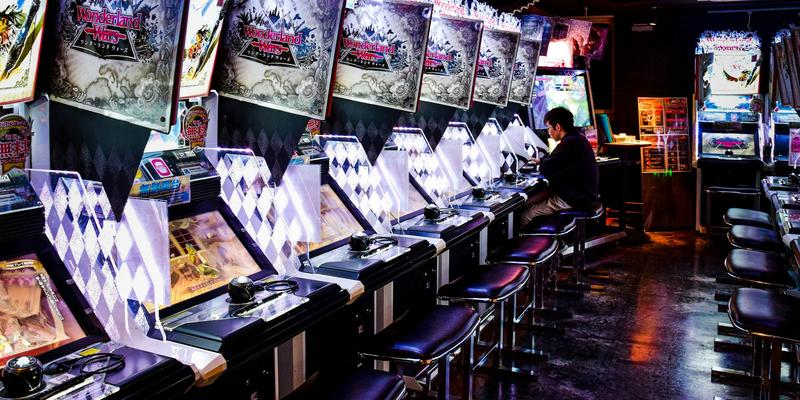 A man plays inside a modern arcade in Tokyo, illuminated by neon lights and gaming machines.