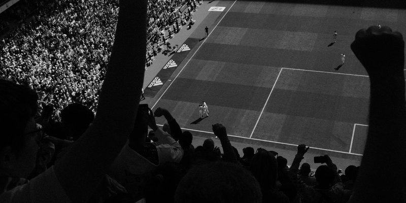 Fans cheering during a high-energy soccer match with players on the field, captured in black and whi