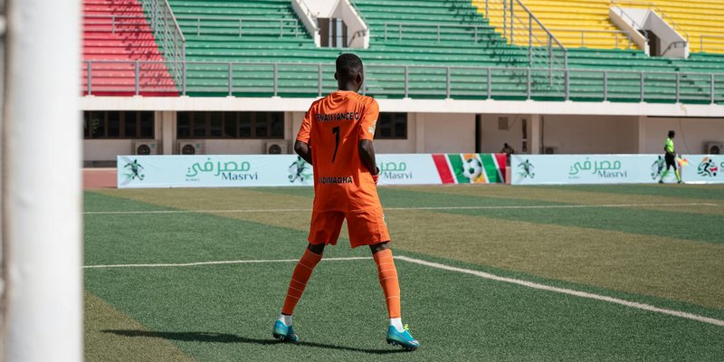 Soccer player in orange uniform on colorful stadium field during daytime game.