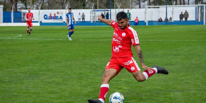 Soccer player in red jersey kicks ball during intense outdoor match.