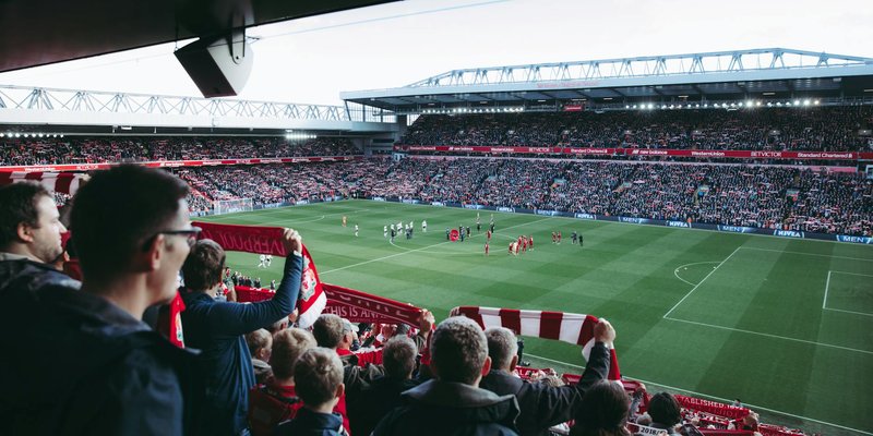 Fans cheer as players take the field at a vibrant football stadium, creating an electric atmosphere.