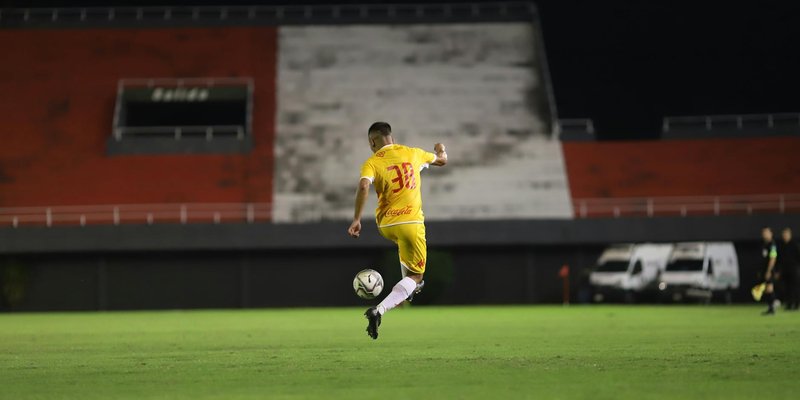 Soccer player in yellow jersey kicking a ball on a green pitch during night match under lights.