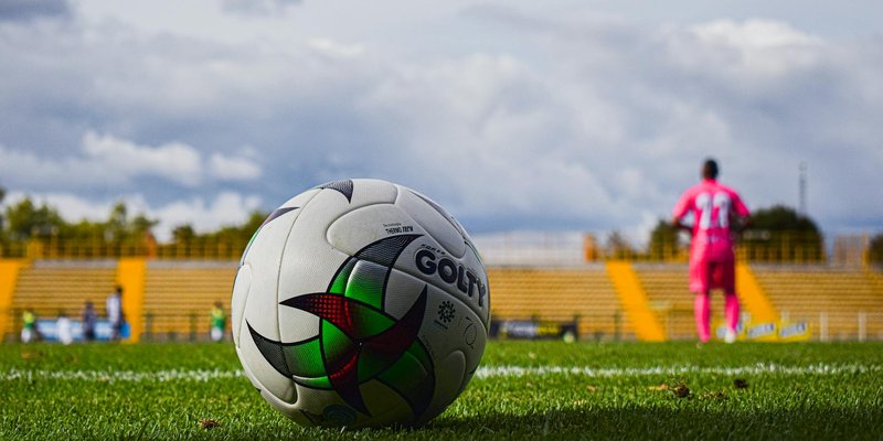 Close-up of a soccer ball on green grass field with a blurred player in pink jersey in the backgroun
