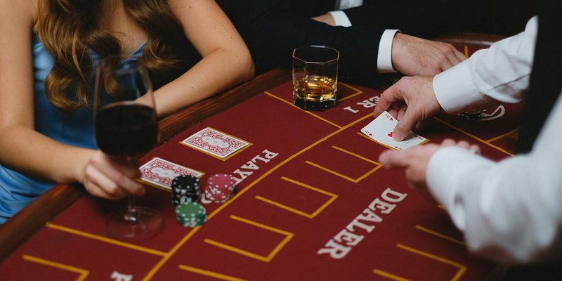 Close-up of a card game with players and chips at a casino table, featuring wine and whiskey glasses