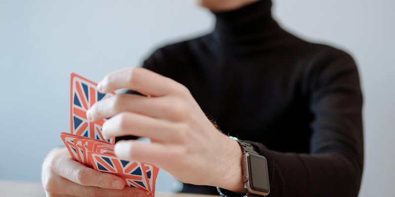 Close-up of a person with a smartwatch playing a card game with British flag cards. Focus on hands.
