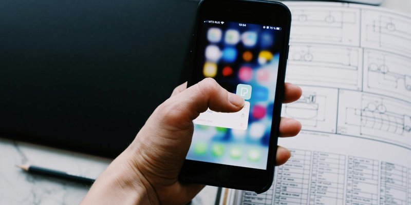A hand holding a smartphone, showcasing a blurred app interface in an office setting.