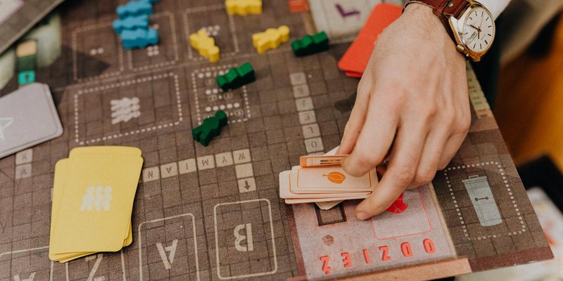 Close-up of a hand playing a board game with cards and colorful pawns.