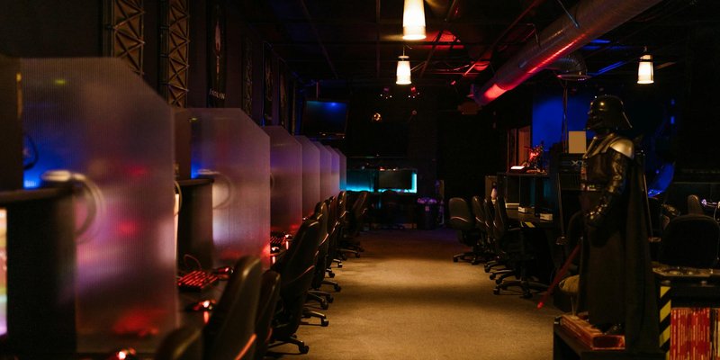 A dimly lit gaming arcade with neon lights and computers, creating a futuristic atmosphere.
