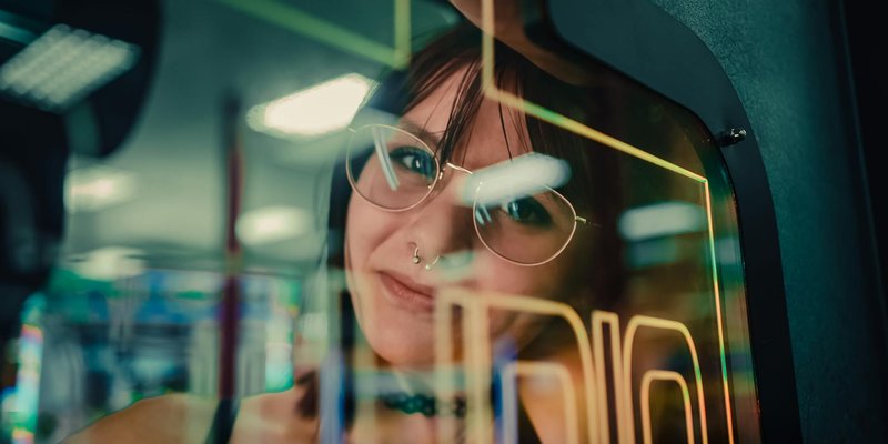 A woman reflected in arcade machine glass, enveloped in neon lights.