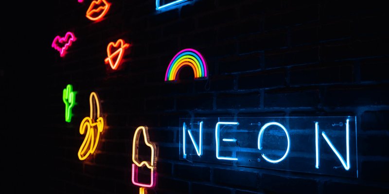 Vibrant neon signs illuminated on a dark brick wall with various shapes and colors.