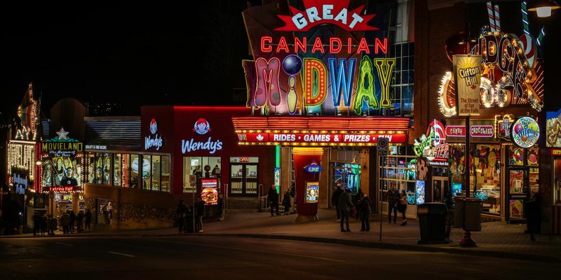 Colorful neon-lit street scene at night featuring the Great Canadian Midway.