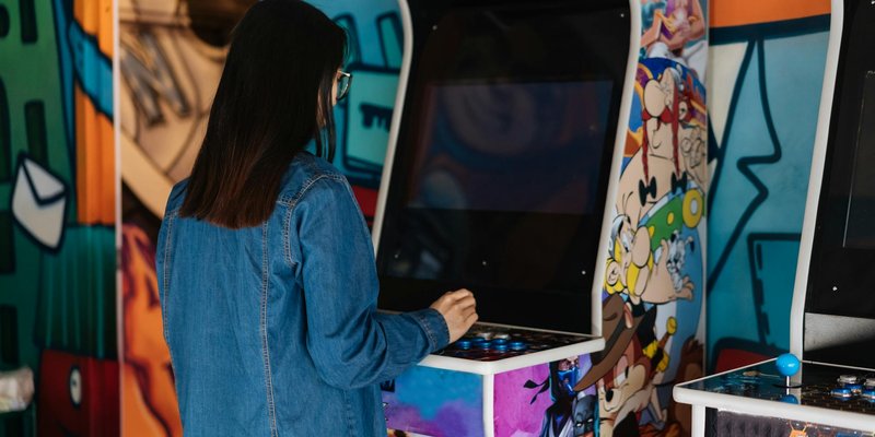 A woman with long hair plays a retro arcade game indoors, enjoying classic gaming fun.